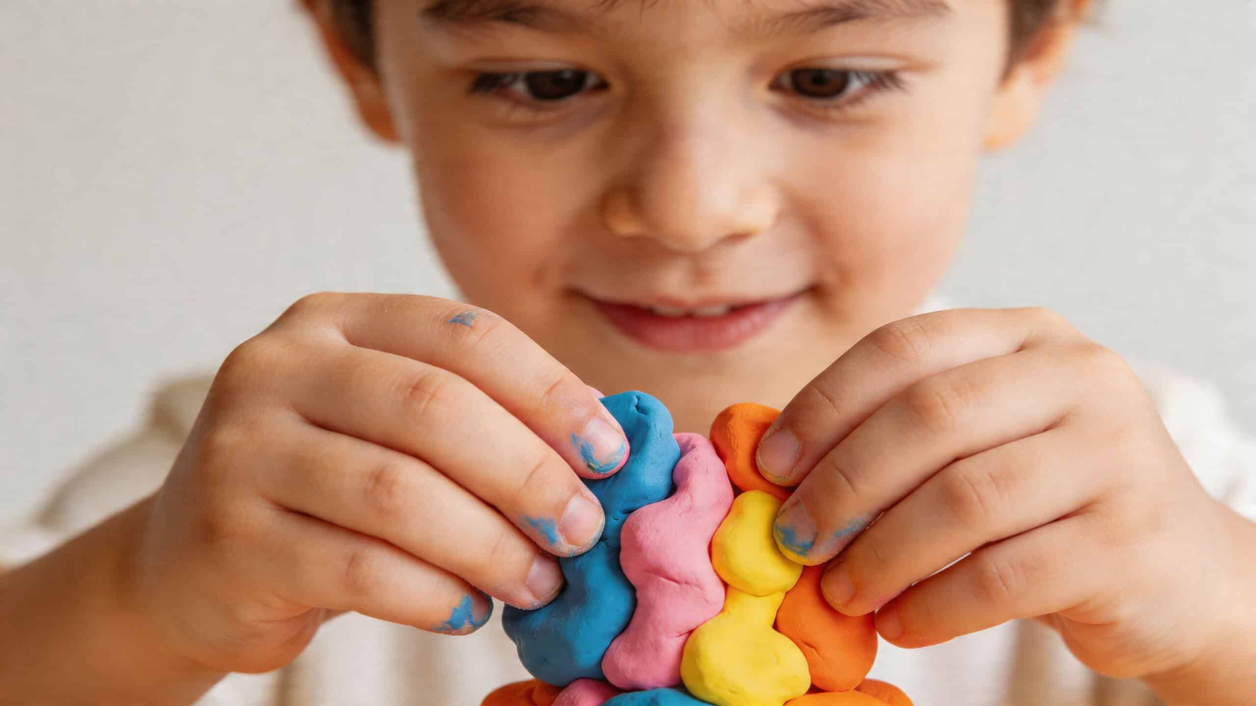 Een jong kind met een vrolijke glimlach speelt geconcentreerd met felgekleurde boetseerklei in verschillende vormen.